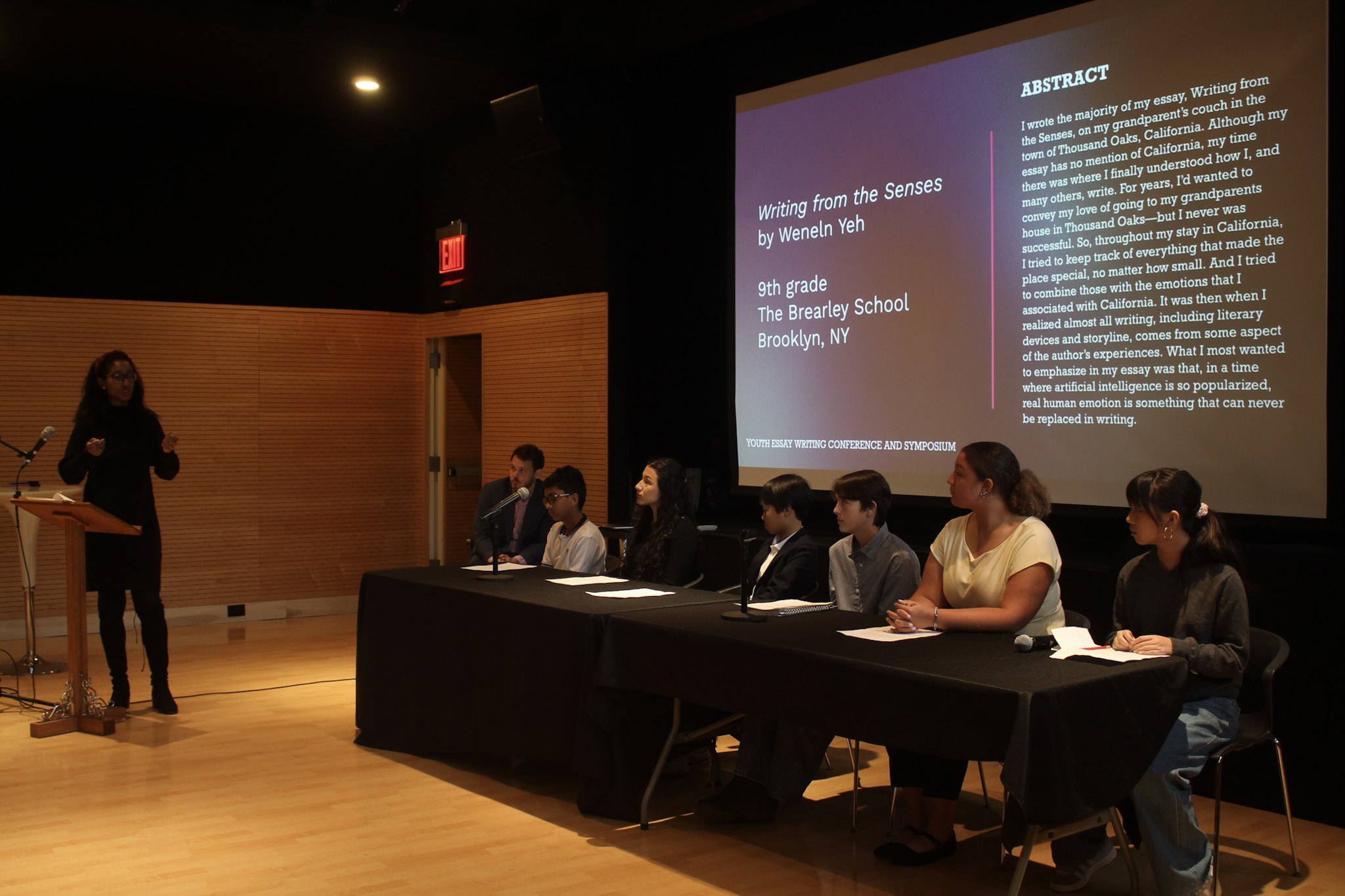 Woman speaking in front a panel of writers