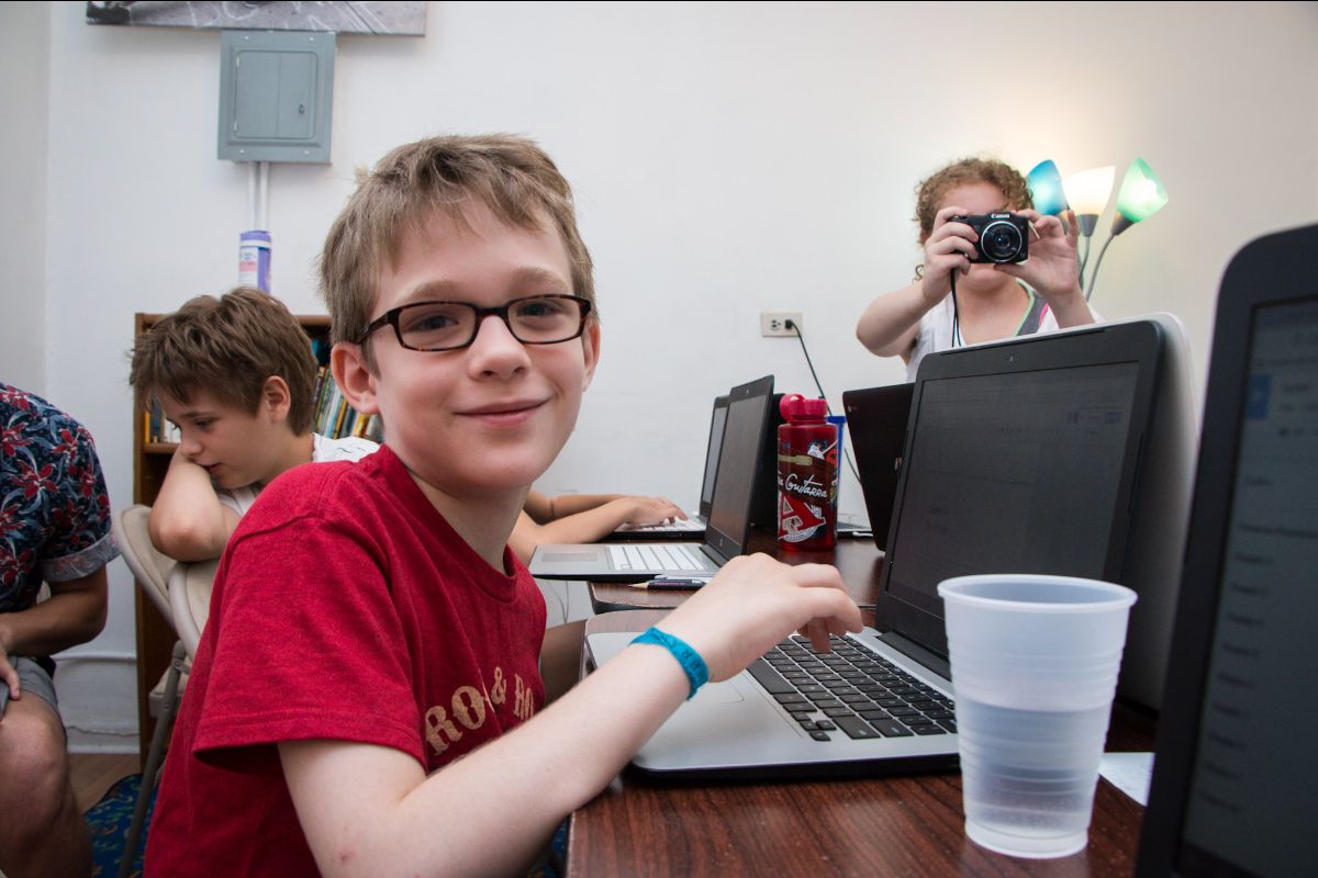 Middle school boy smiling and writing a story on a laptop.