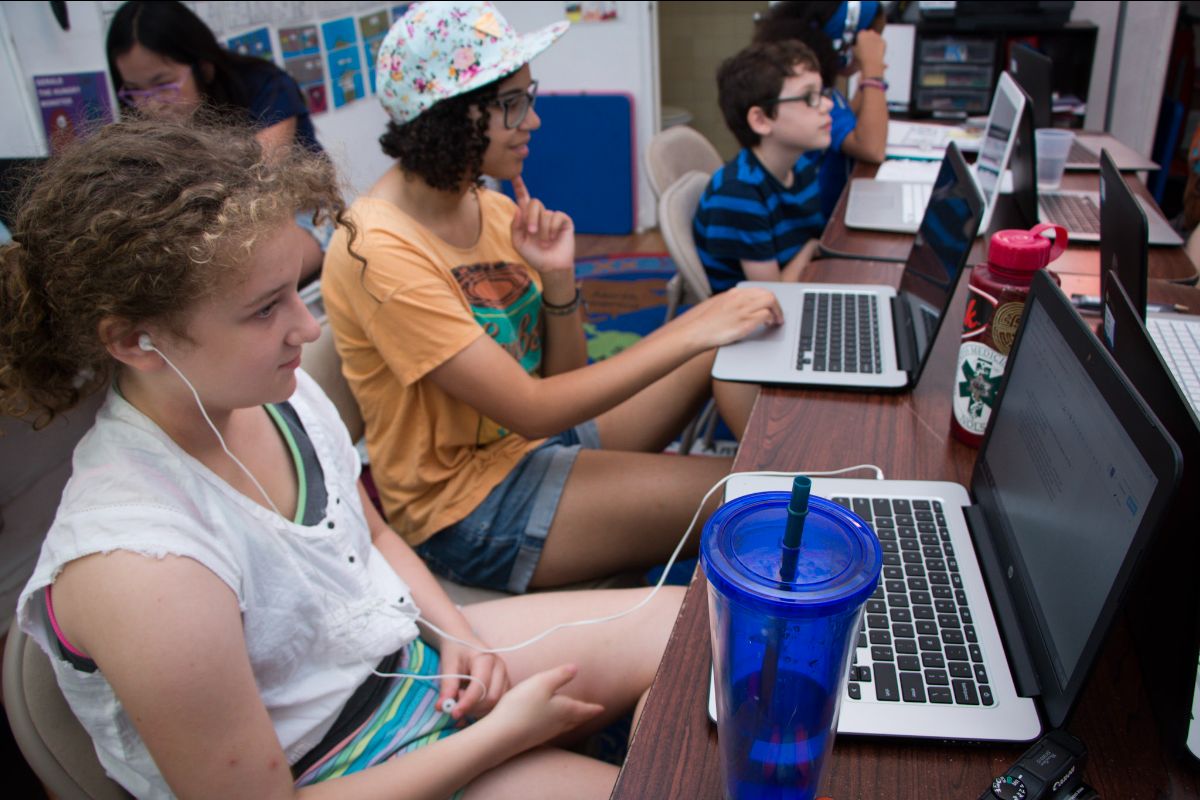 Three kids working diligently writing on laptops.